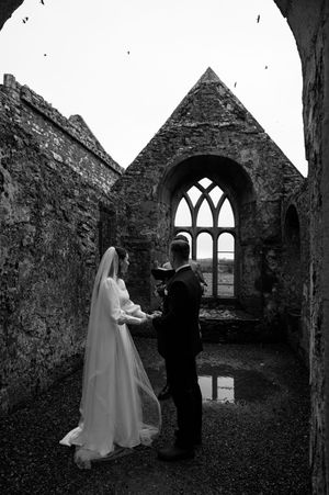 Gothic wedding photoshoot in dramatic black and white at a ruined medieval church with arched windows.