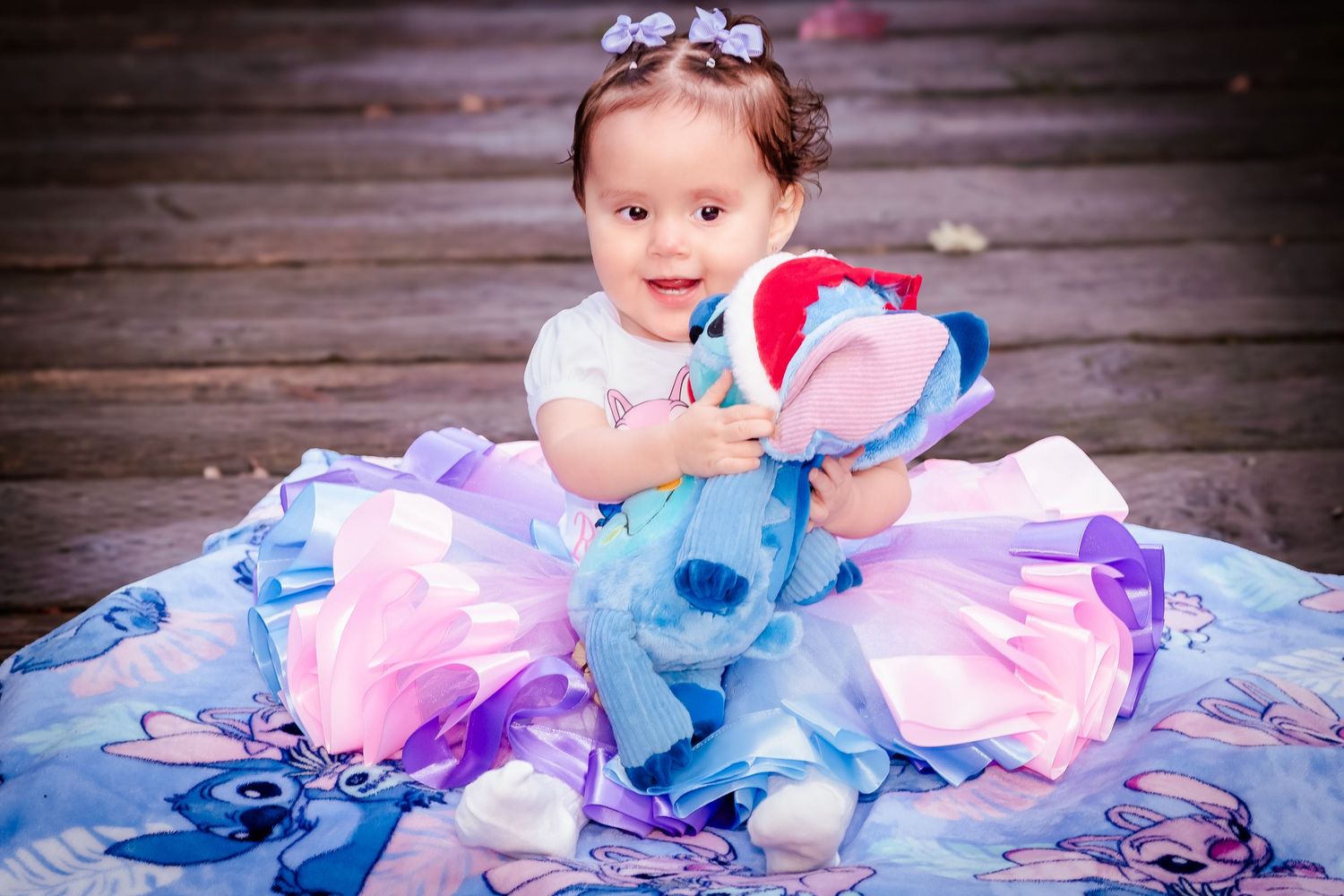 Toddler girl in a blue and pink tutu dress holds a Stitch plush toy while sitting on a Lilo and Stitch blanket.