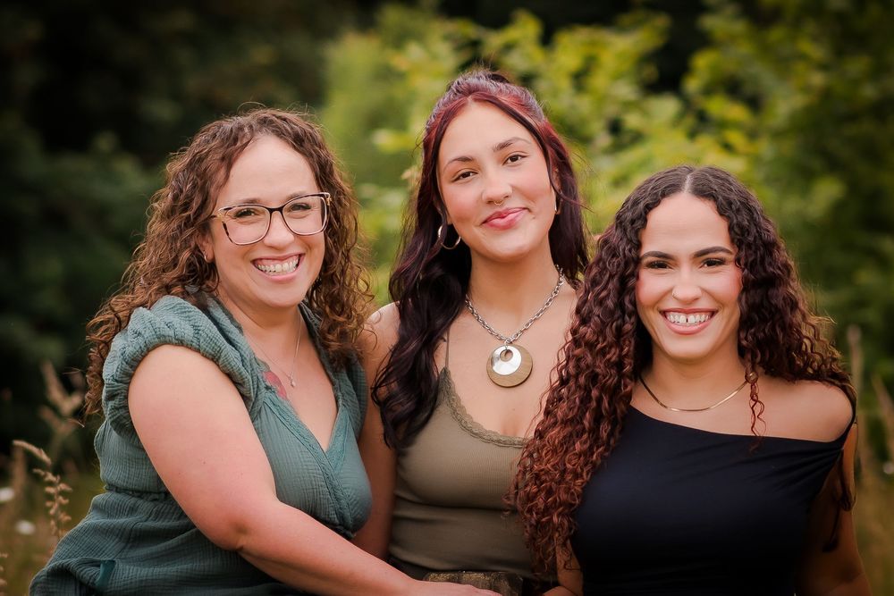 Three people smile warmly while posing together outdoors in natural setting.