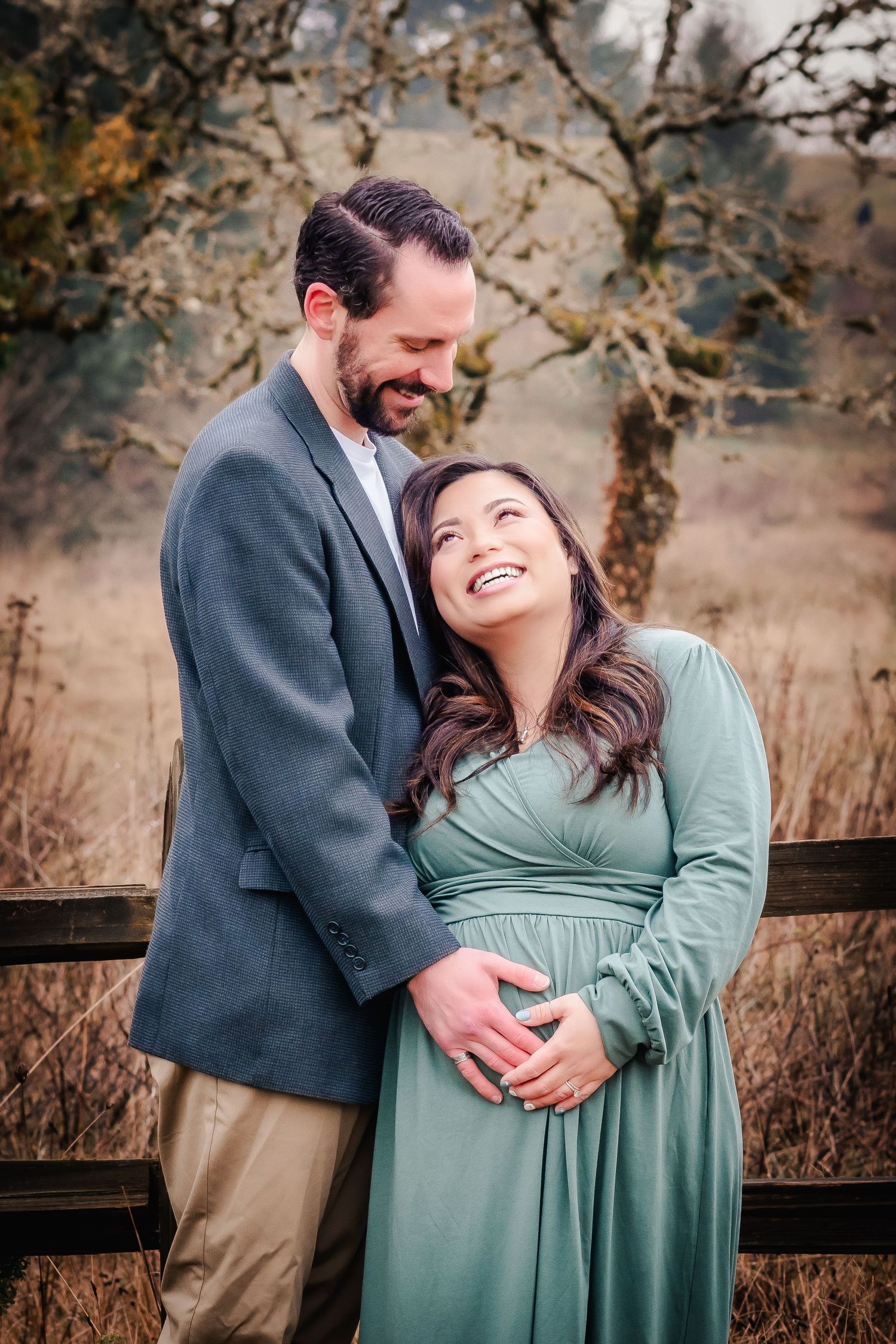 Couple sharing a joyful moment outdoors, woman in green dress cradling baby bump.
