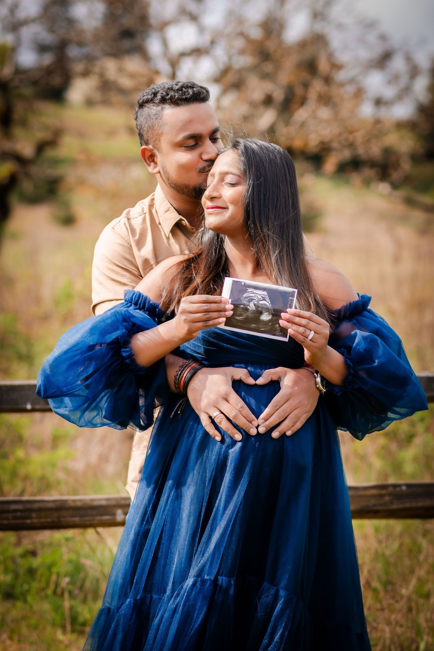 A couple in matching blue outfits embrace and smile while taking photos outdoors in a natural setting.