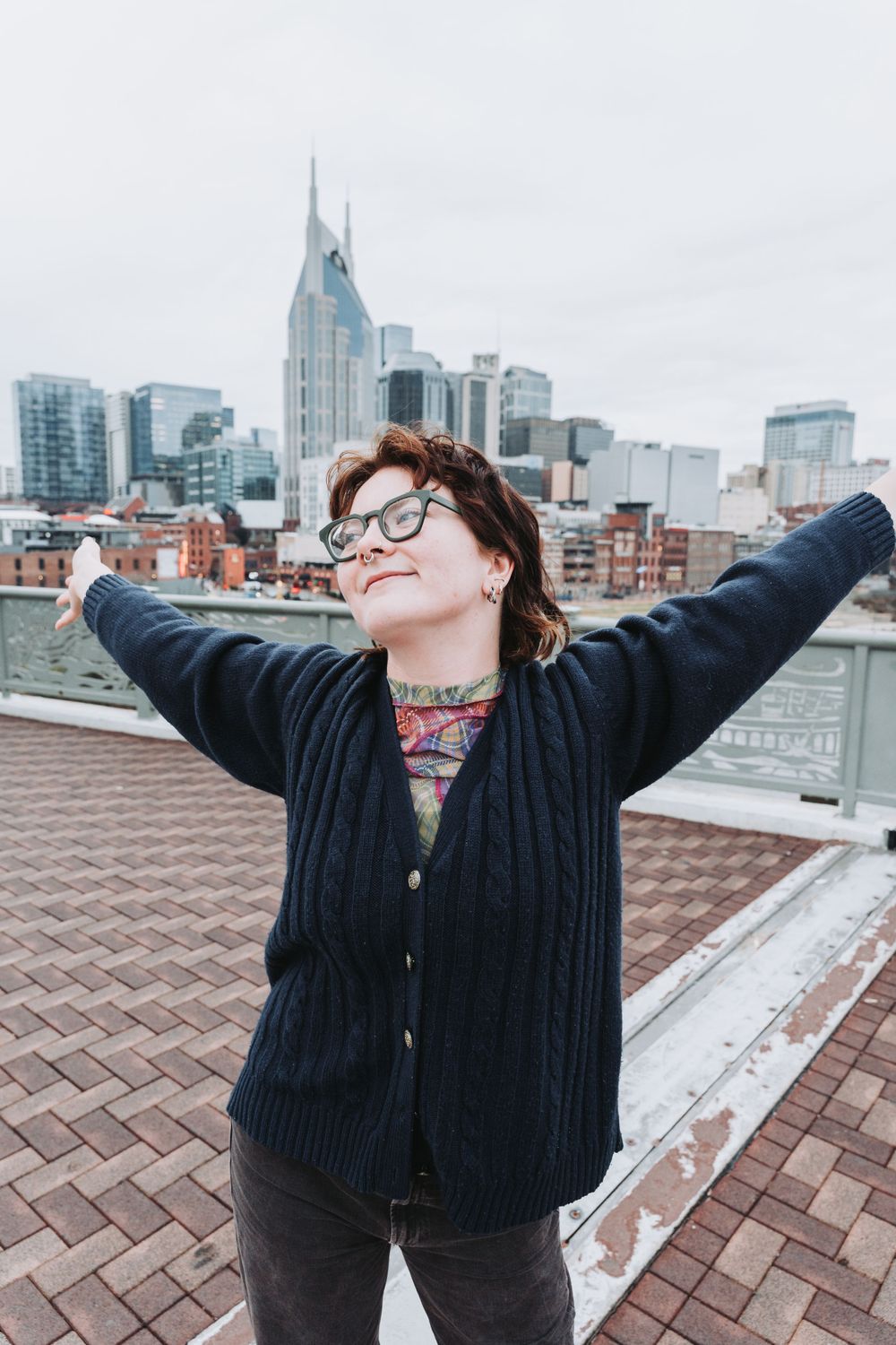 A person stretches their arms wide with joy on a rooftop overlooking the Nashville city skyline on a cloudy day.