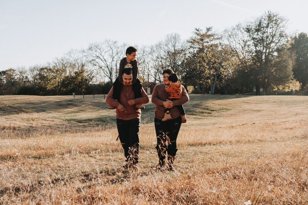 Group of people running together through a golden field at sunset with bare trees in the background.