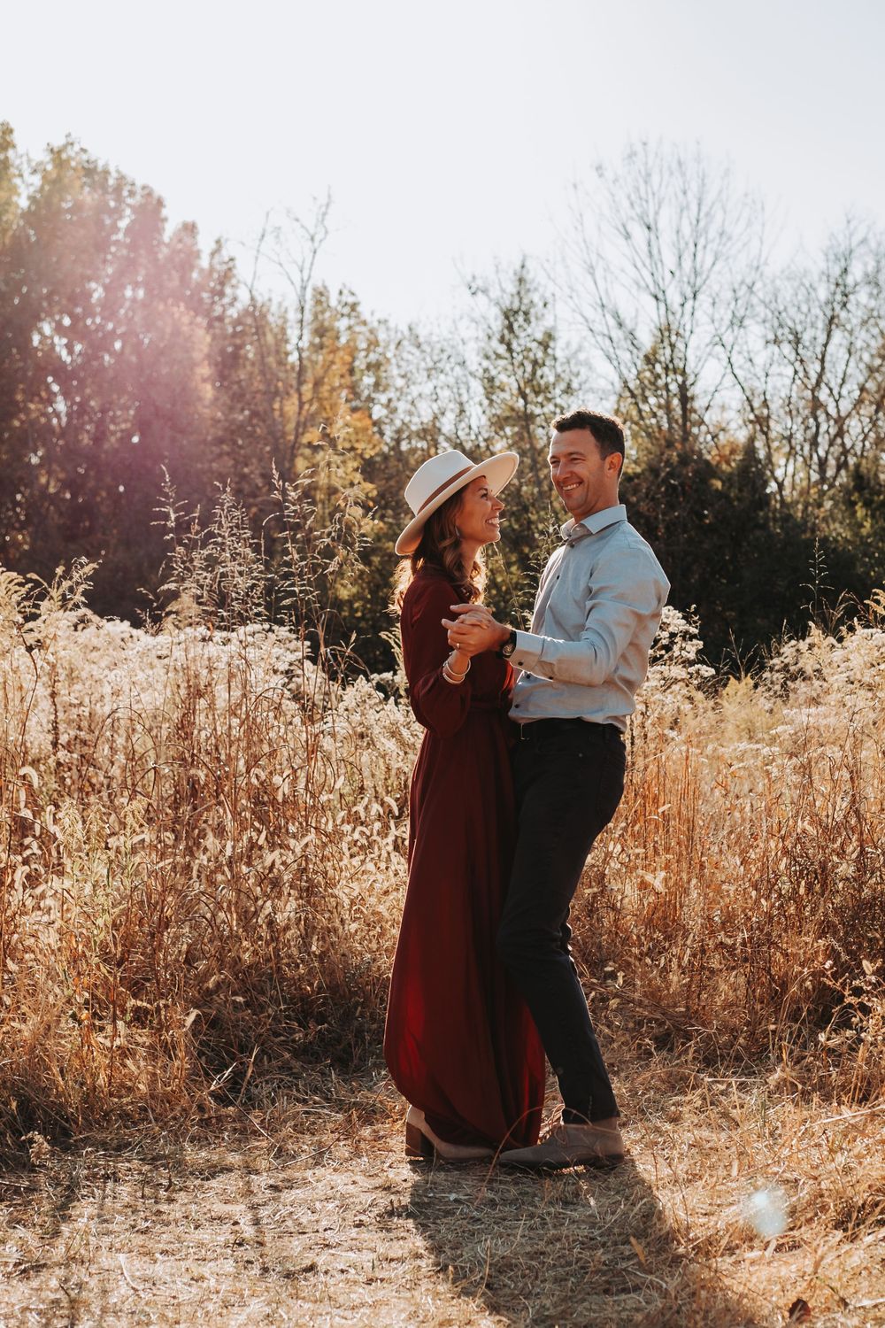 A couple embraces in a golden sunlit field with tall dried grass during autumn.