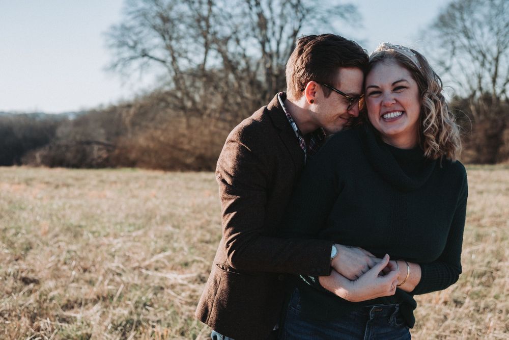 A couple shares an intimate moment together while standing in a sunlit autumn field.