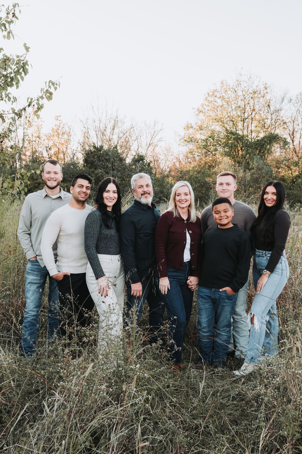 A diverse group of people in casual attire standing together outdoors against an autumn nature backdrop.