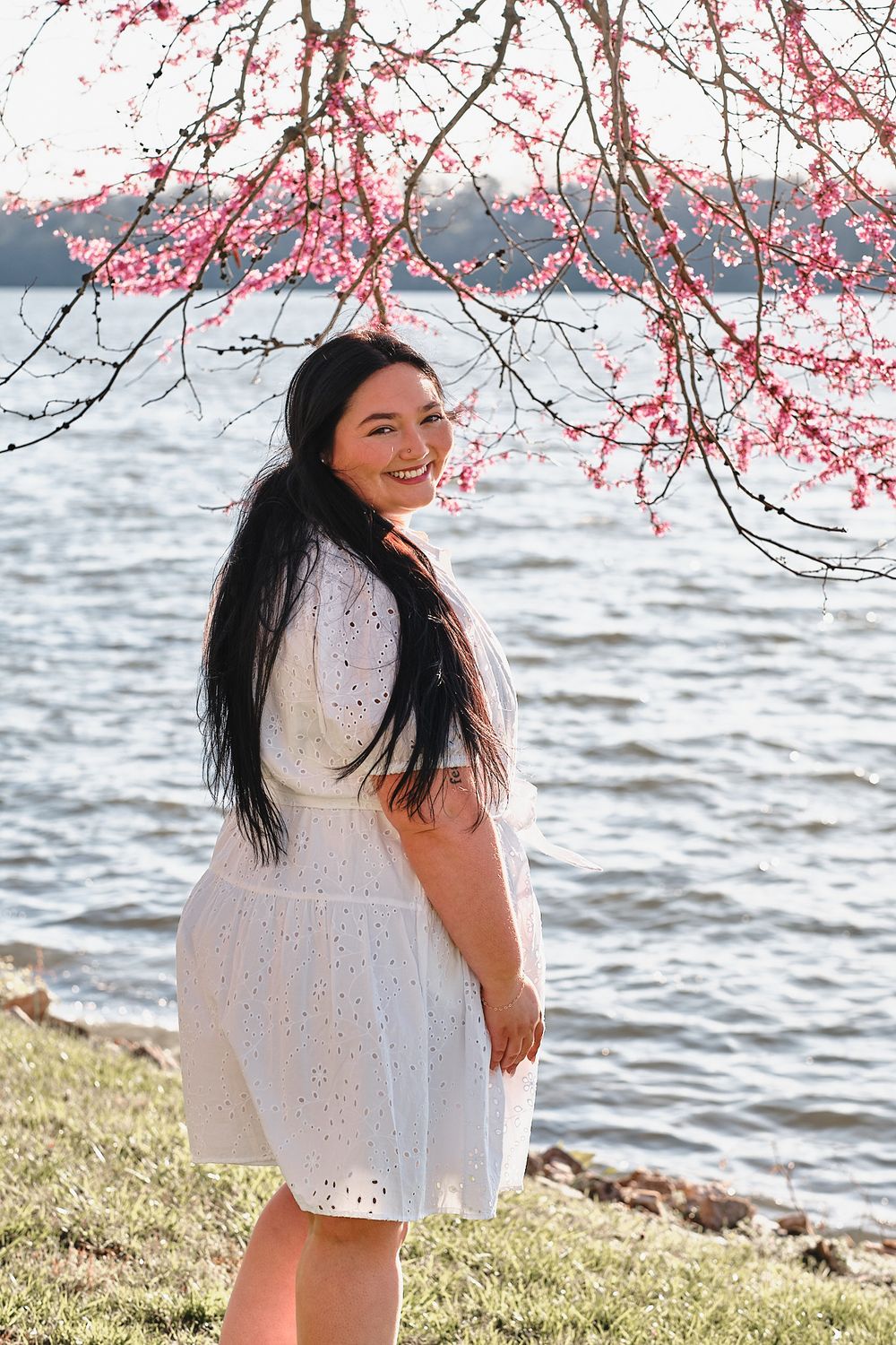 A spring portrait under blooming cherry blossoms beside a waterfront.