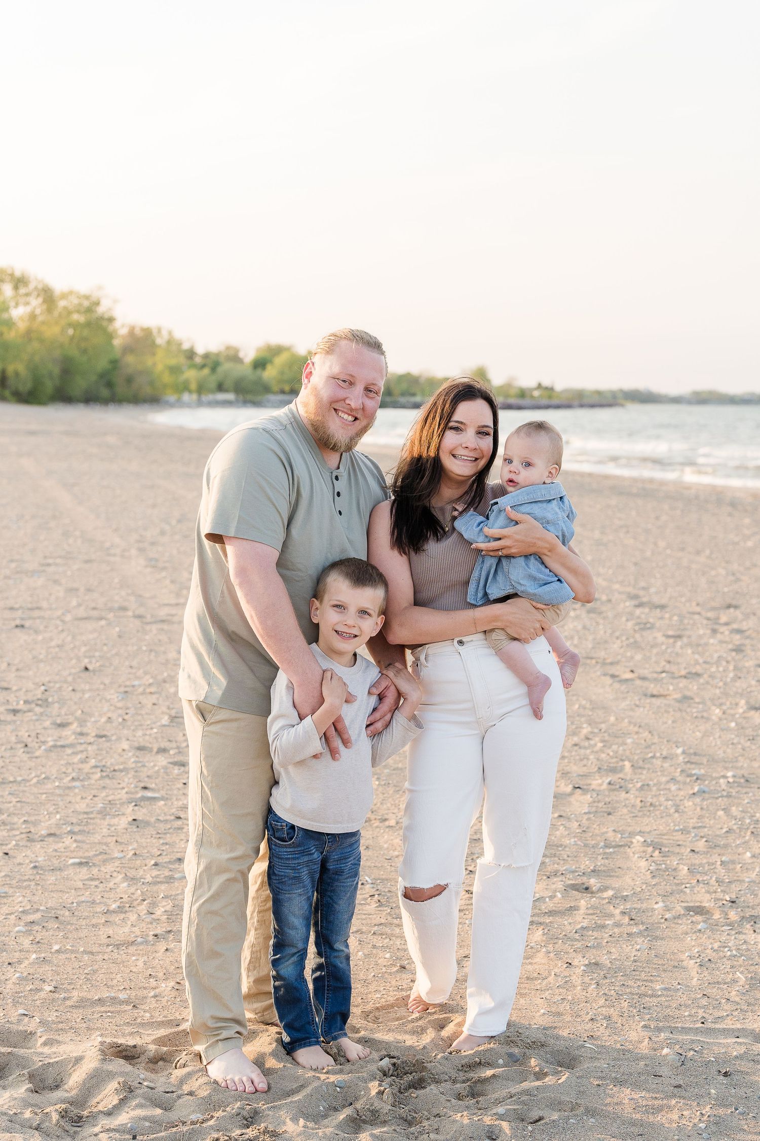 Happy family of four posing together on a sandy beach at sunset.