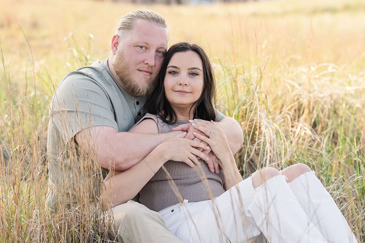 Couple sitting together in a golden field of tall grass during sunset.