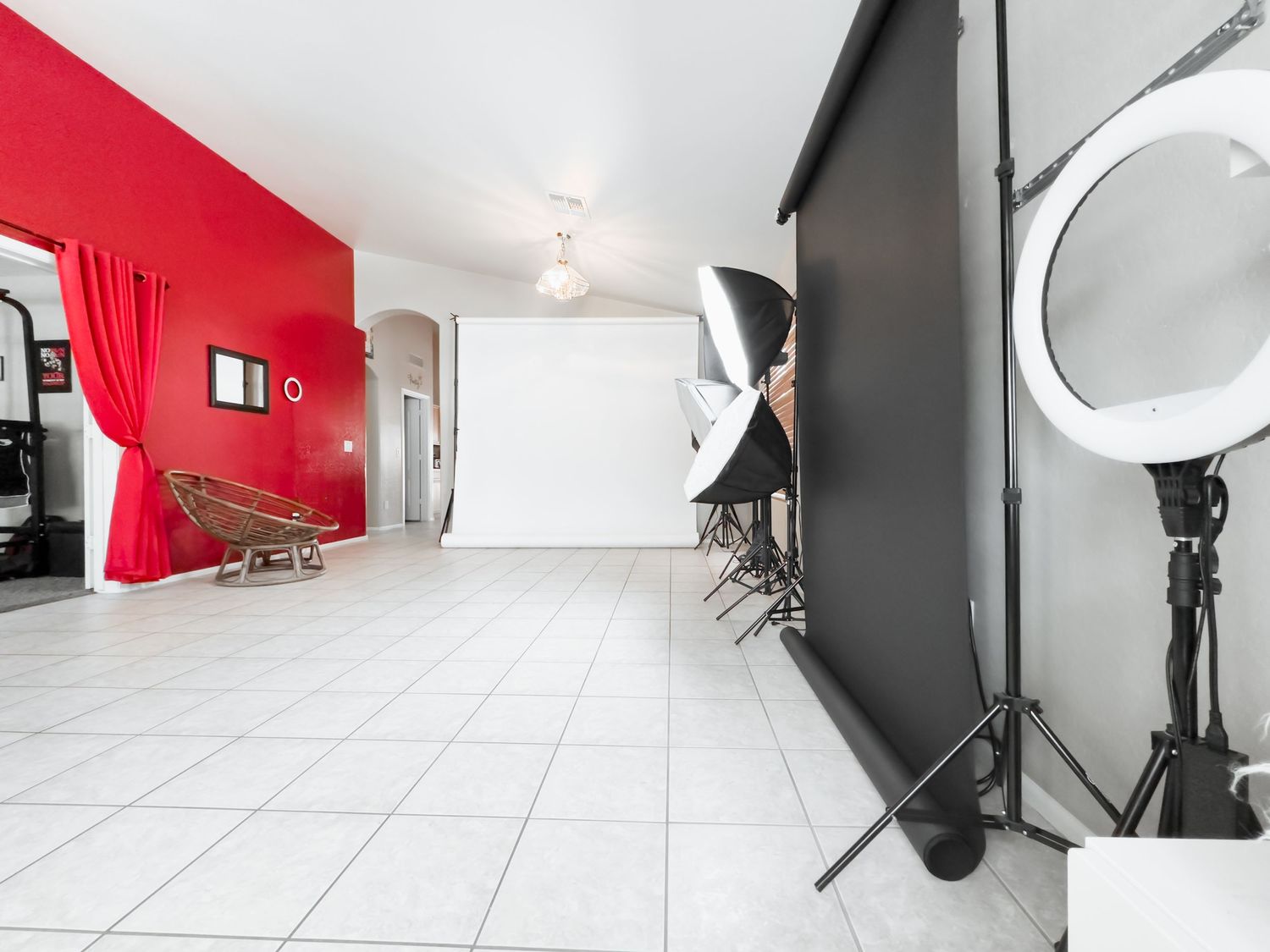 Professional photo studio interior with red accent wall, white backdrop, lighting equipment and tiled floor.