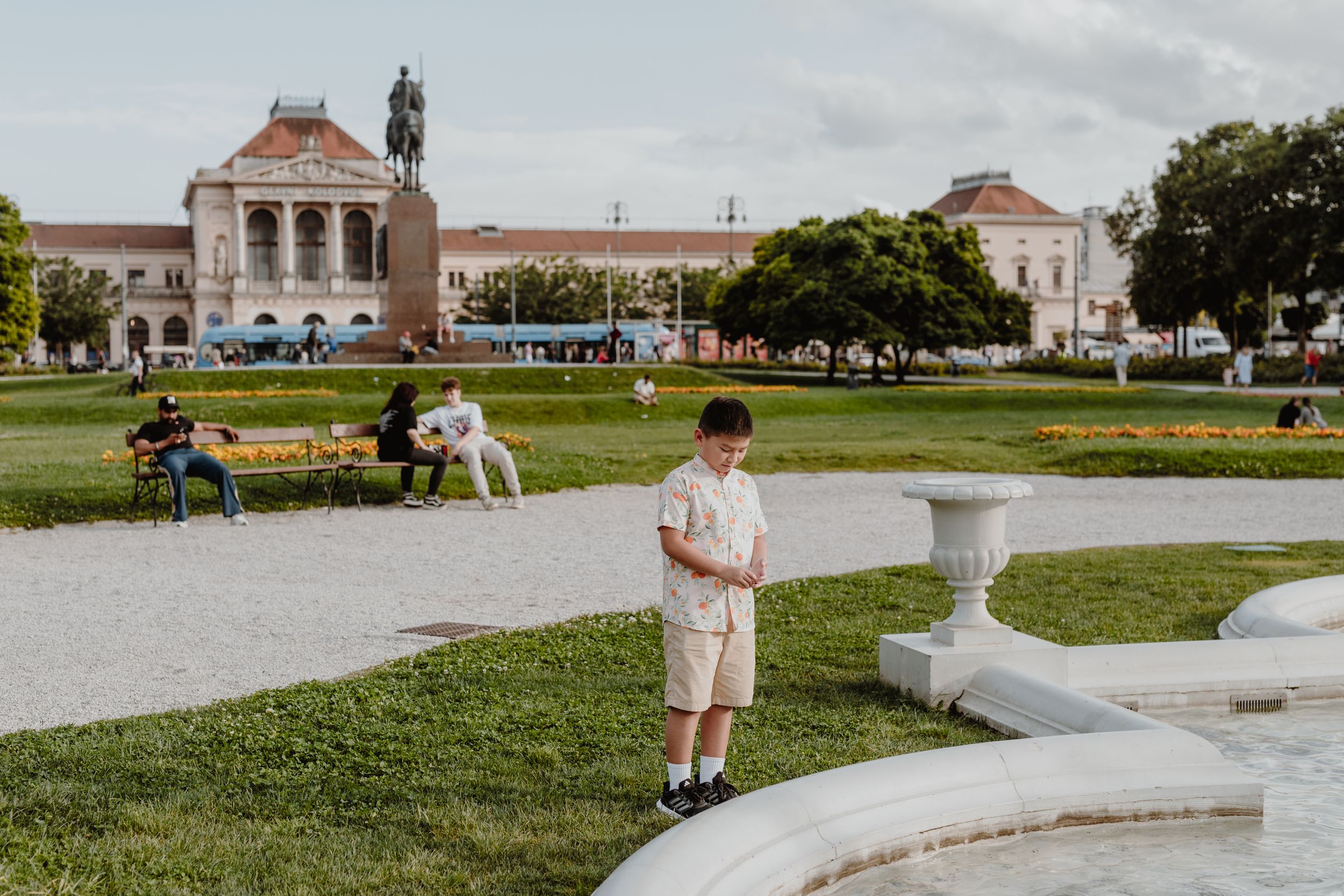 A person stands near a fountain in front of a grand historical building with classical architecture.