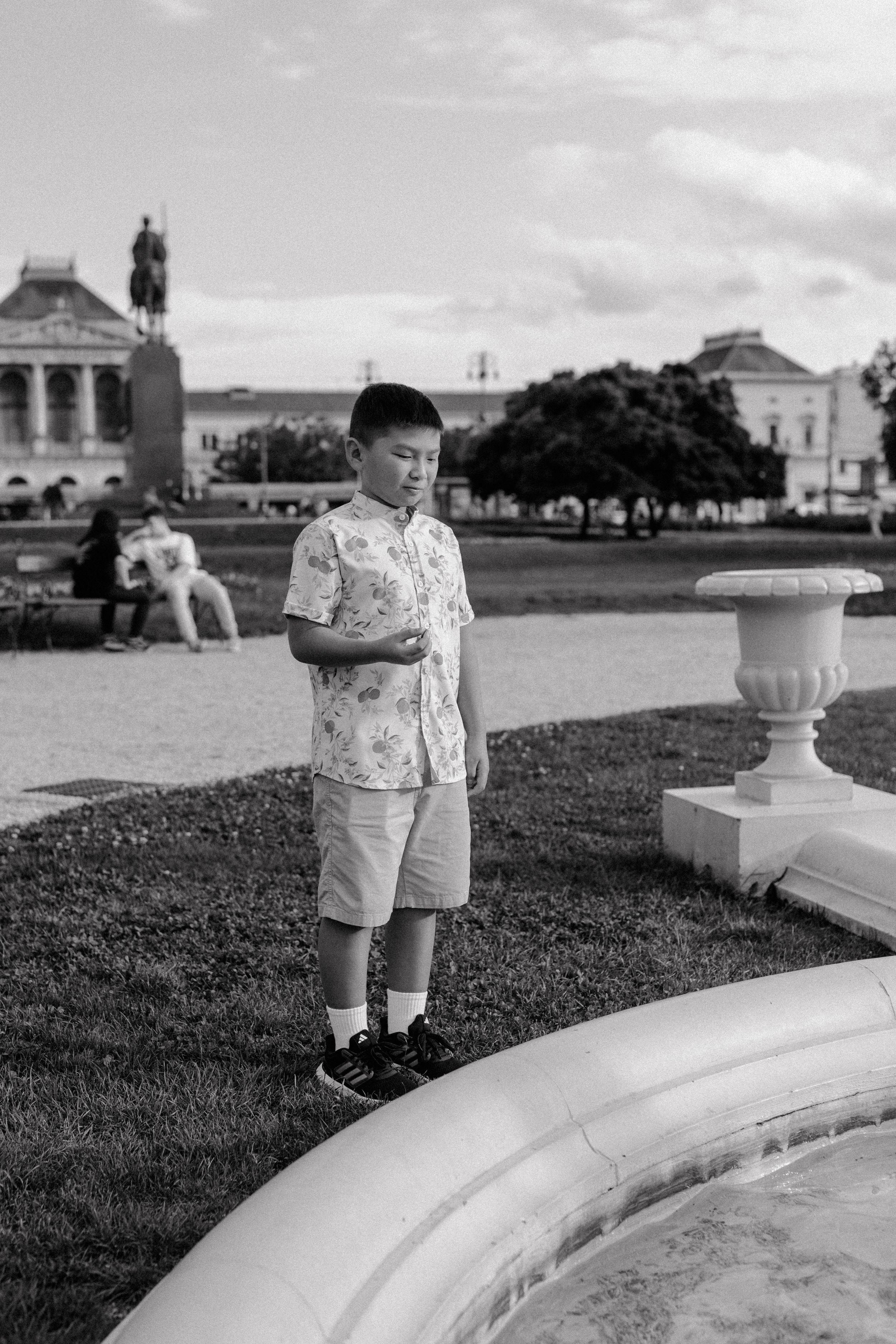 Black and white photo of someone by a fountain at a historic European-style plaza.