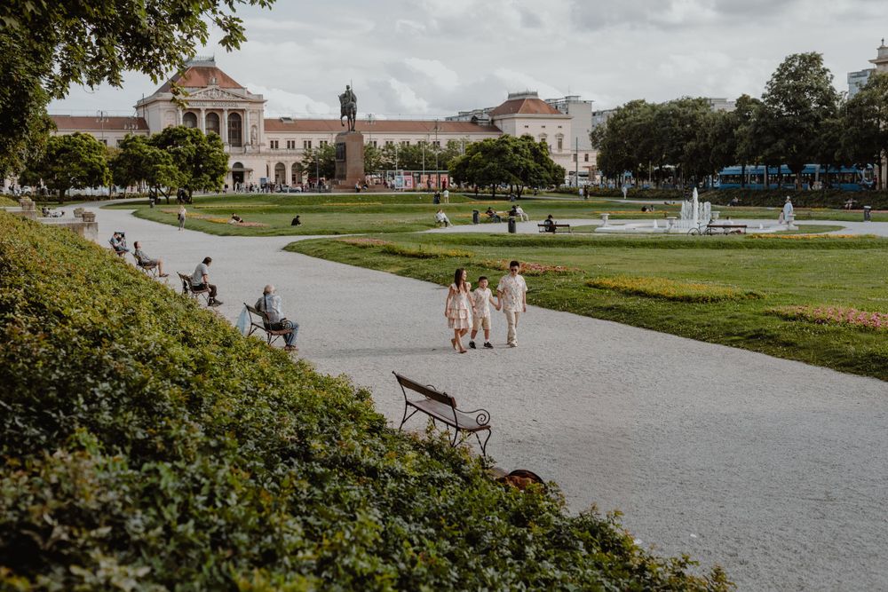 People in coordinated outfits walking along a path in a manicured garden with classical buildings.