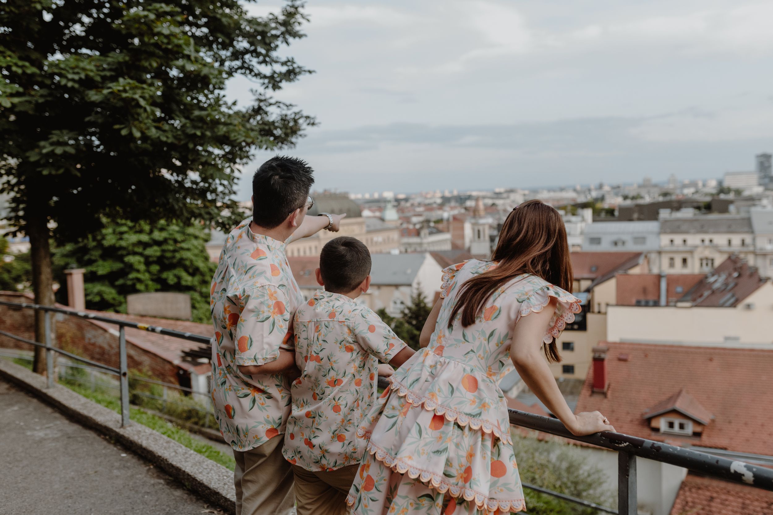 "Family standing together with their 10-year-old, viewed from behind, with the Zagreb skyline in focus in the background