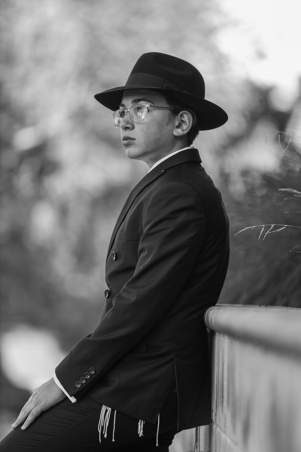 Young man in black suit and fedora hat leaning on railing, black and white photo.