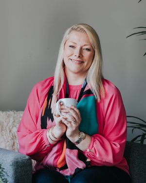 Someone relaxes on a couch in a pink sweatshirt while holding a coffee mug.