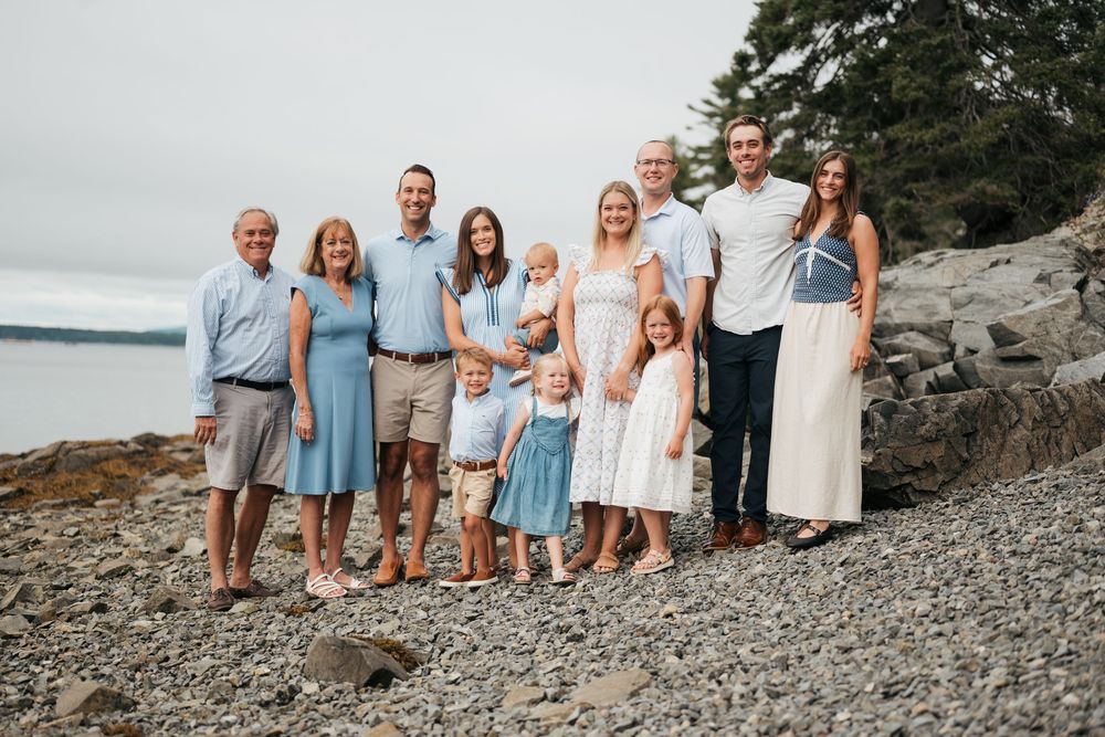 Large multigenerational family portrait on rocky beach with overcast sky in Bar Harbor, Maine.
