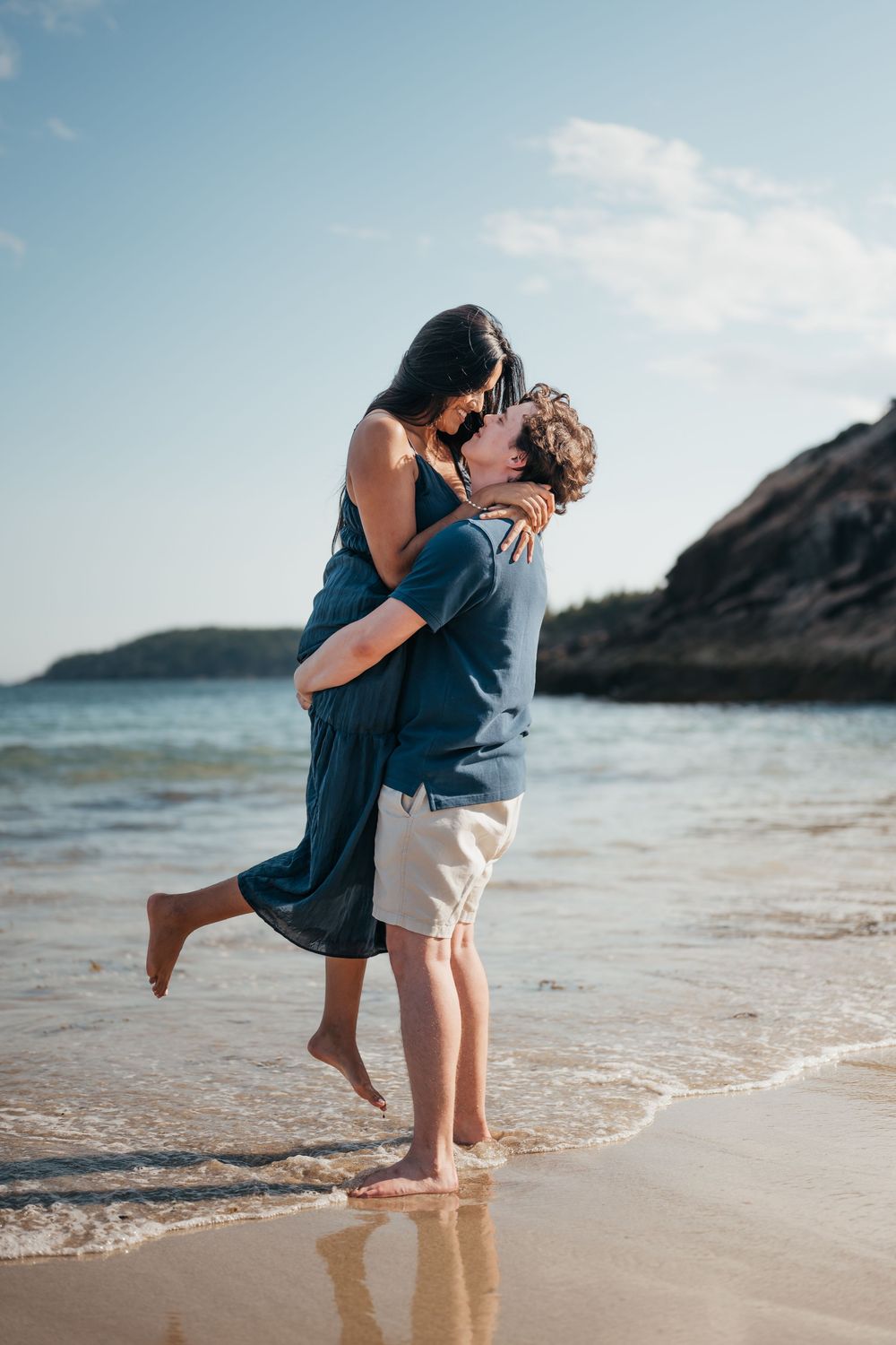 Romantic couple embracing and kissing on sandy beach with ocean waves.