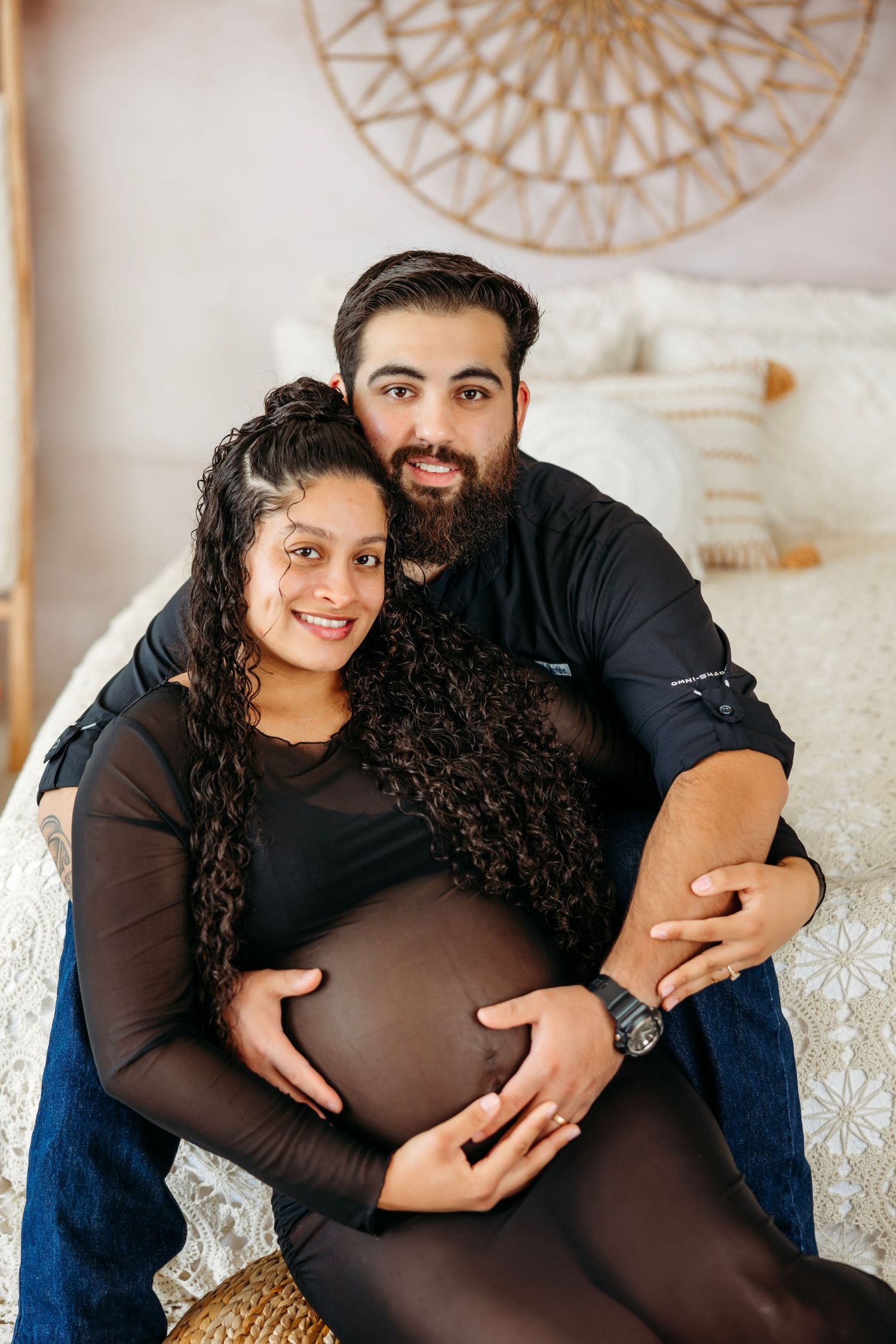 A maternity photo series showing a couple in black and blue outfits posing together against a white decorative background.