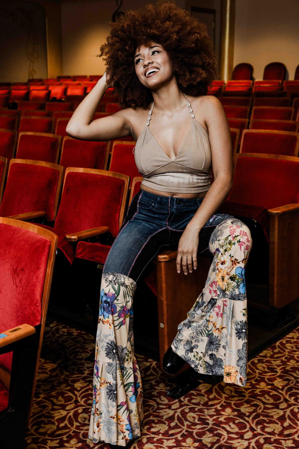 Model with natural afro hair poses in theater wearing floral bell-bottom jeans.