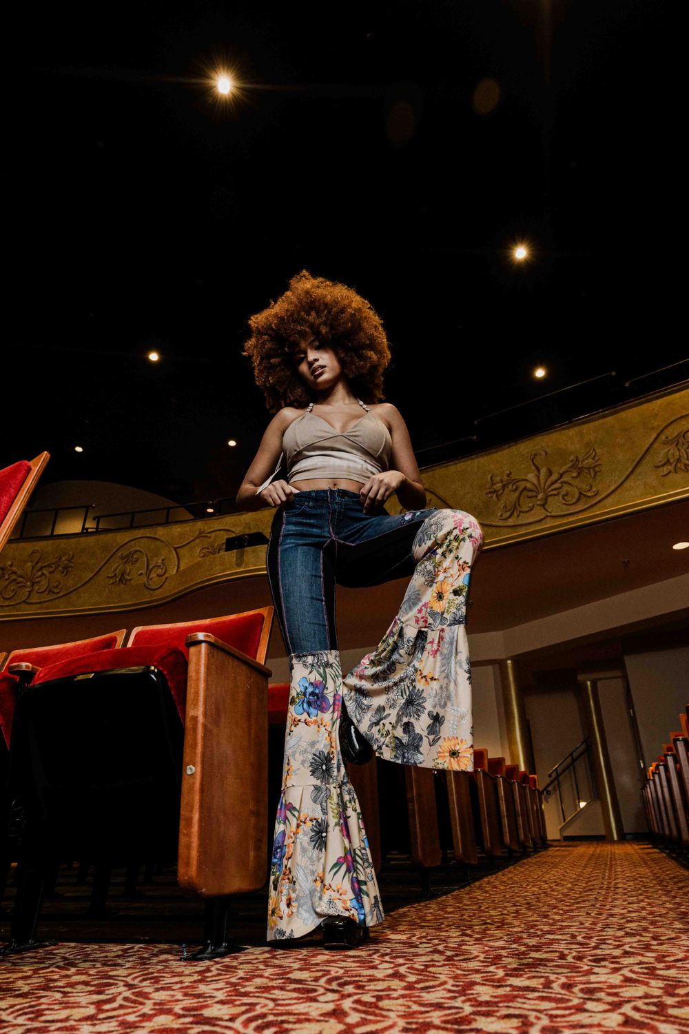 Dramatic low-angle shot in theater showing floral bell-bottom jeans and tank top.