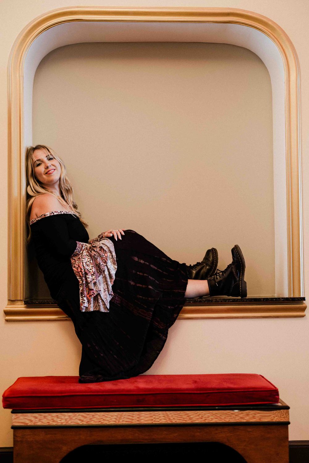 Person in black dress reclines in arched wall nook with red cushioned bench.