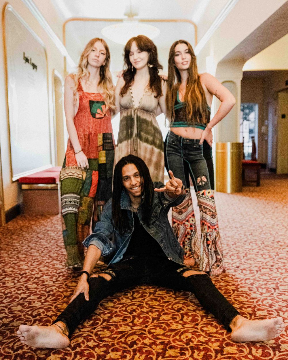 Friends pose together in colorful boho outfits against patterned carpet.