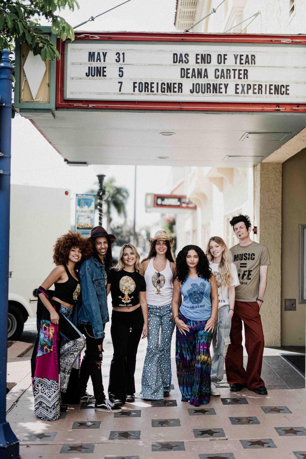 Group of young people standing beneath a theater marquee displaying upcoming show dates.