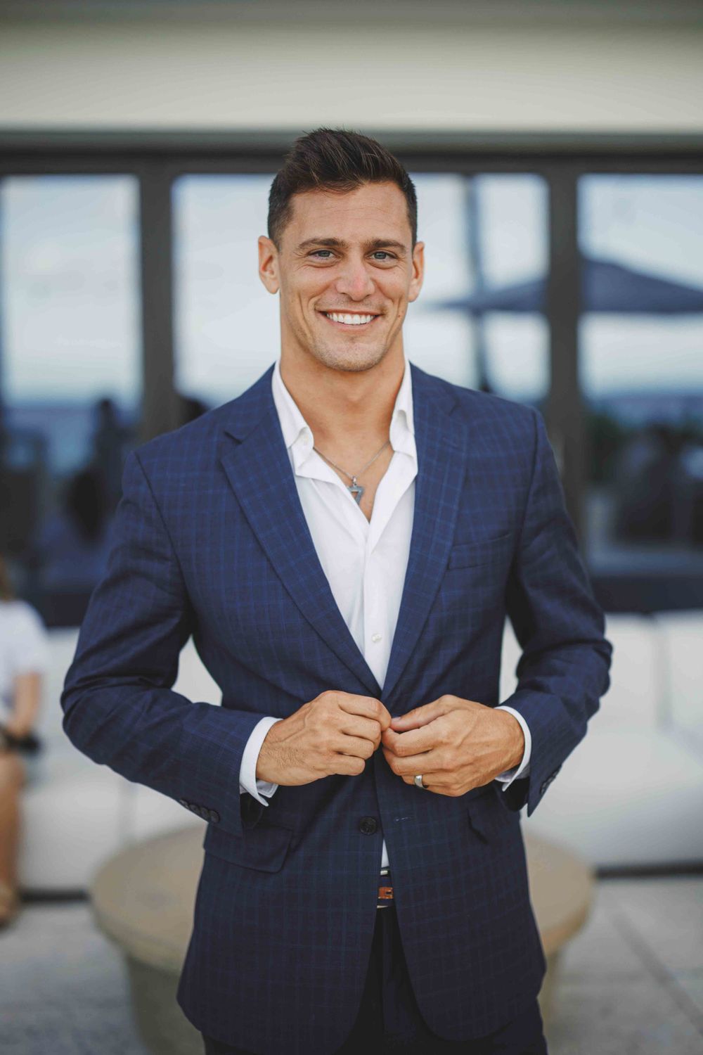 Professional in navy suit and white shirt poses in modern business setting.