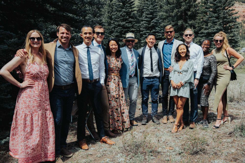 Group photo of wedding guests standing together against a backdrop of evergreen trees.