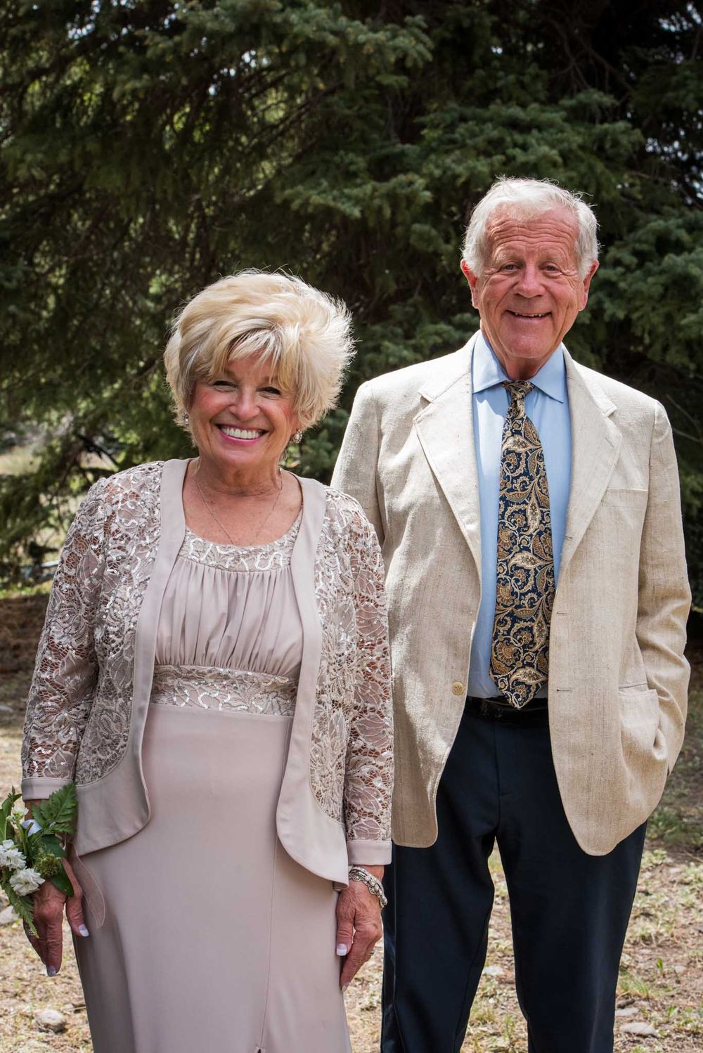 Elegant couple in formal attire pose together at an outdoor event.