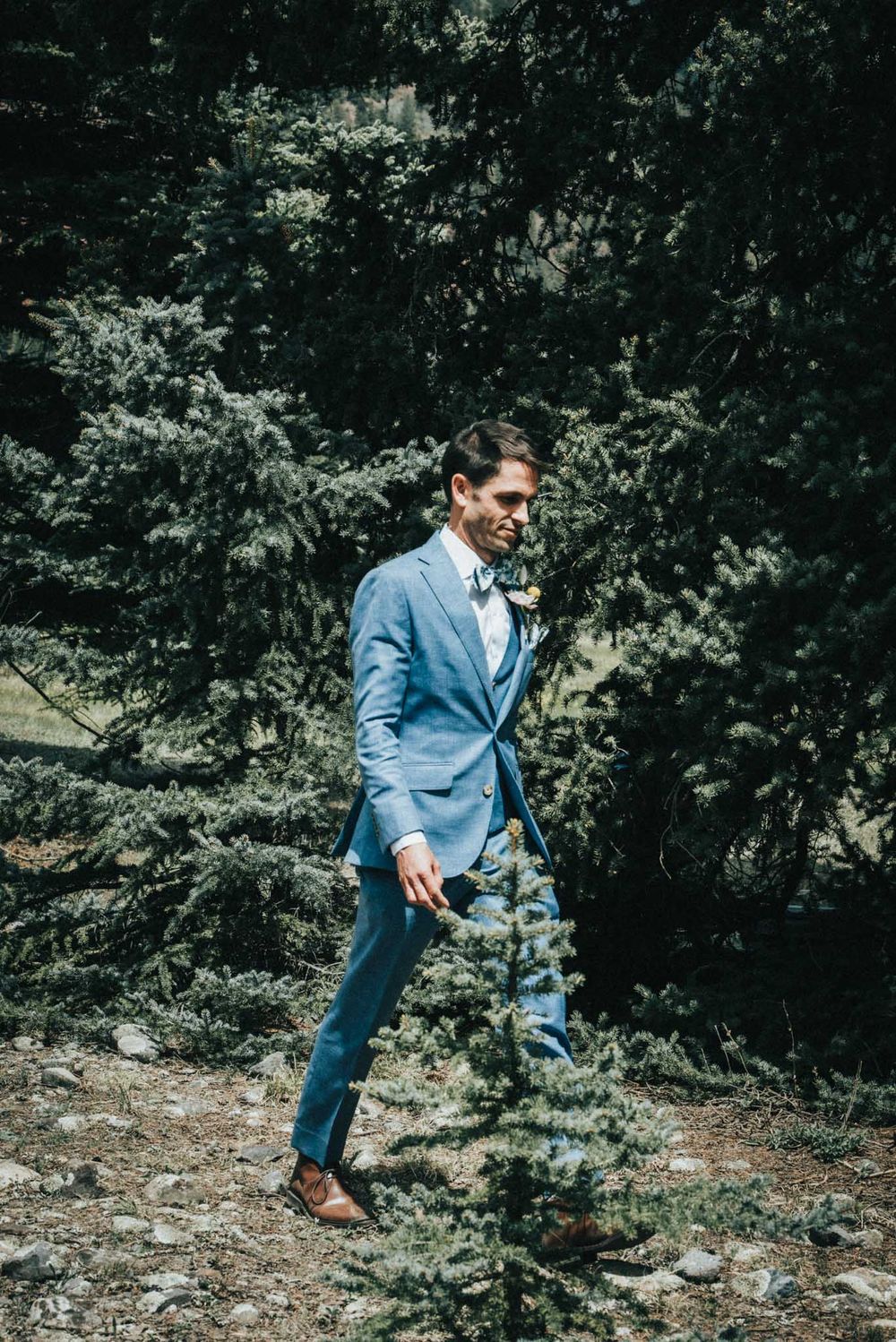 Man in blue suit walking outdoors with trees in background.