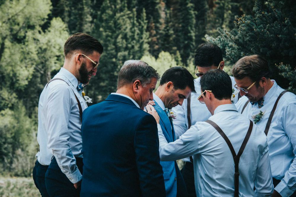 Group of men in formal attire huddle together in prayer or discussion outdoors.