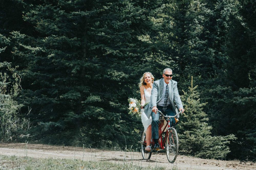 A couple shares a romantic bike ride through a wooded forest path on their wedding day.