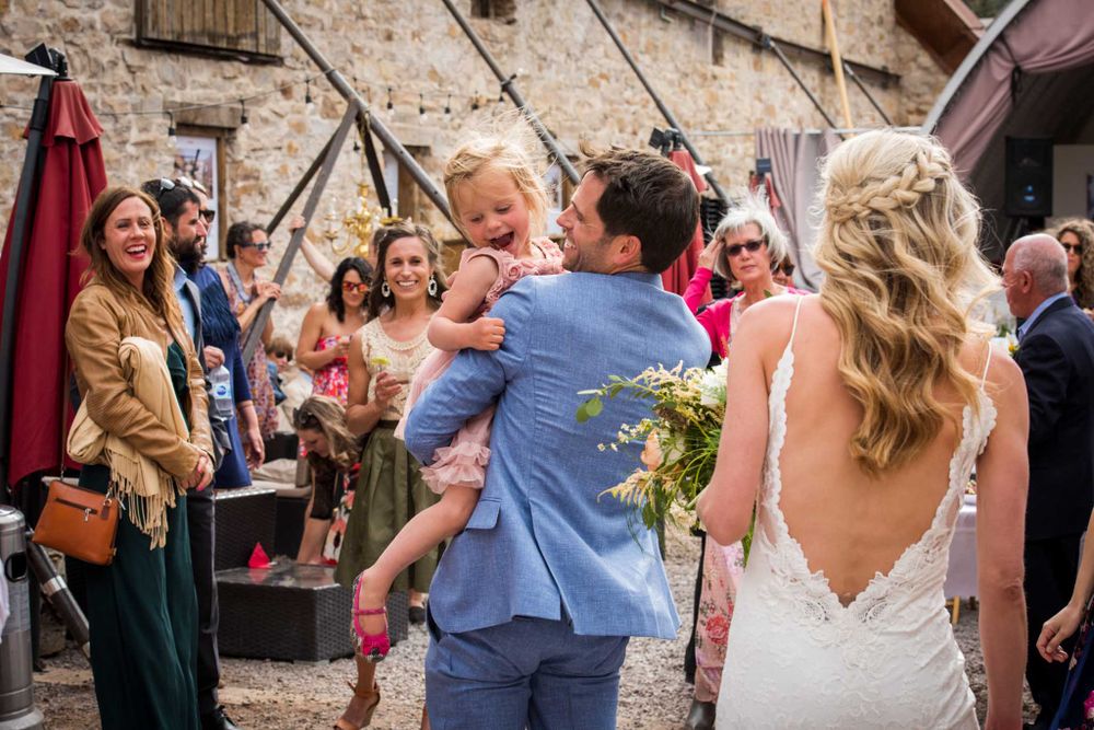 Outdoor wedding celebration with guests gathered around a rustic stone building.