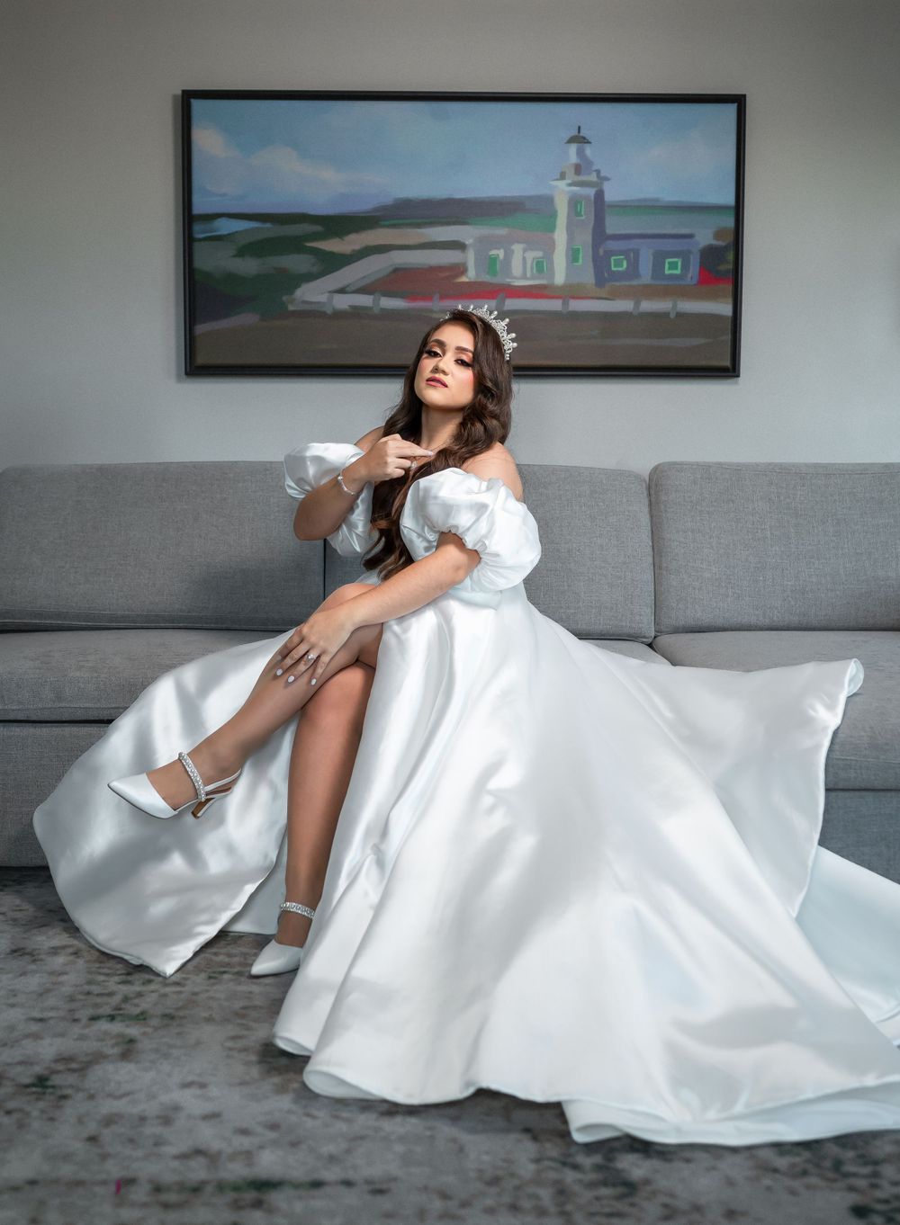 A bridal portrait on a grey couch with a coastal lighthouse painting in the background.