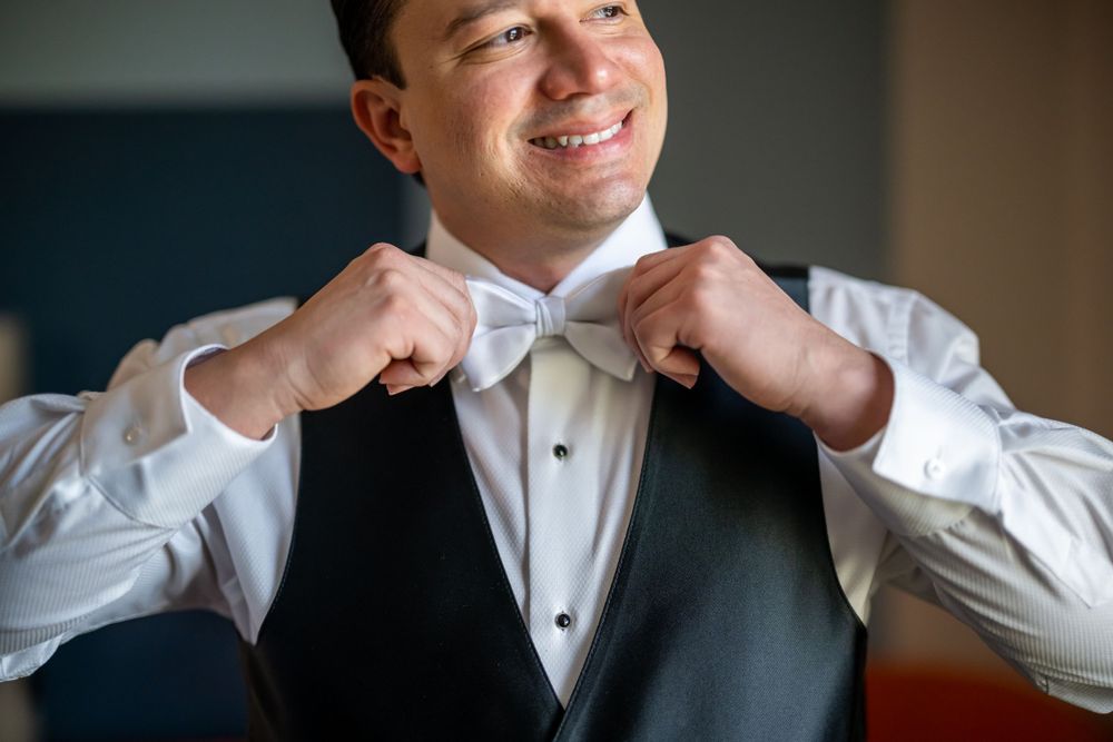 Close-up shot of a tuxedo-clad person adjusting their white bow tie.