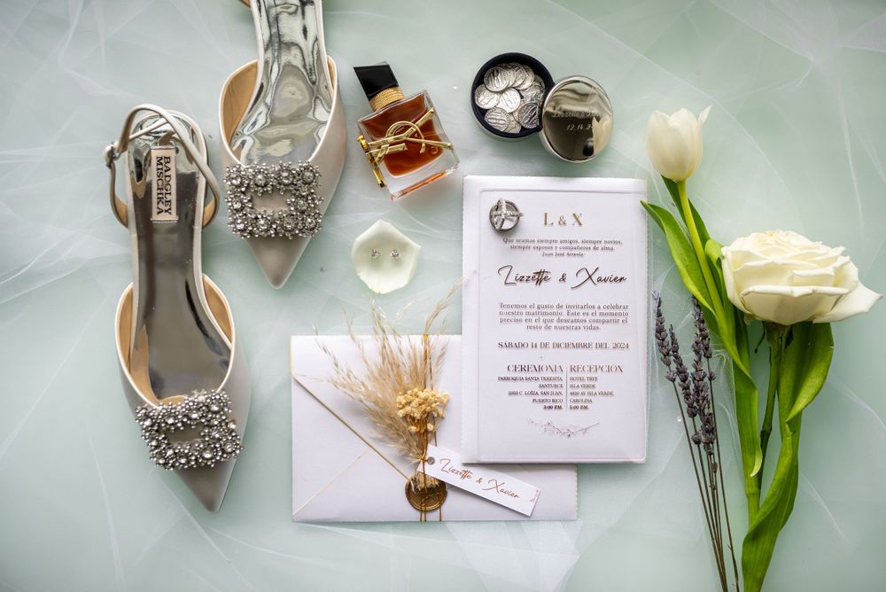 Wedding details including sparkly heels, invitation, perfume, and white roses arranged on a mint green surface.