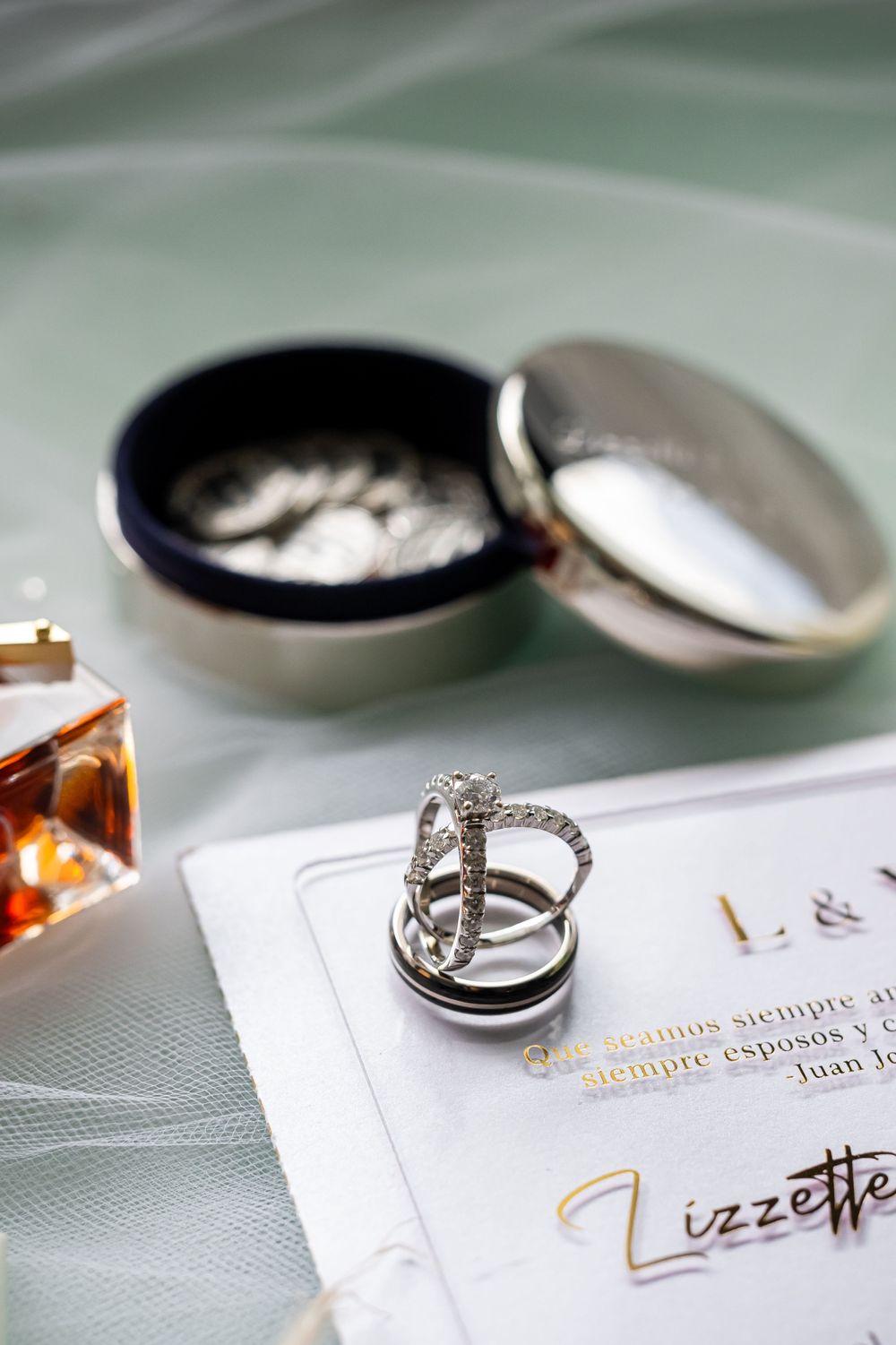 Close-up of an elegant diamond ring with jewelry box and amber perfume bottle on wedding stationery.