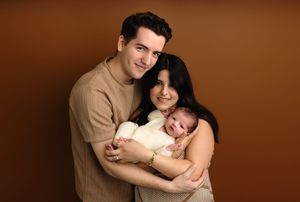 Proud new parents cuddle their baby boy together against a dark brown backdrop, captured by Charlottesville newborn photographer.