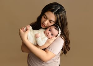 Mother cradles her wide awake baby girl against a beige backdrop, captured by Charlottesville newborn and family photographer.