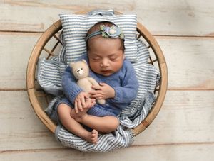 Baby girl in blue knits cradles a teddy bear as she curls up in a basket, captured by Charlottesville and Culpeper newborn photographer.