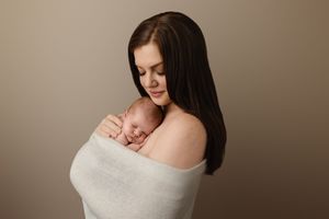 Mom cradles her newborn against her chest, as they are wrapped together in white, by Charlottesville baby and family photographer.