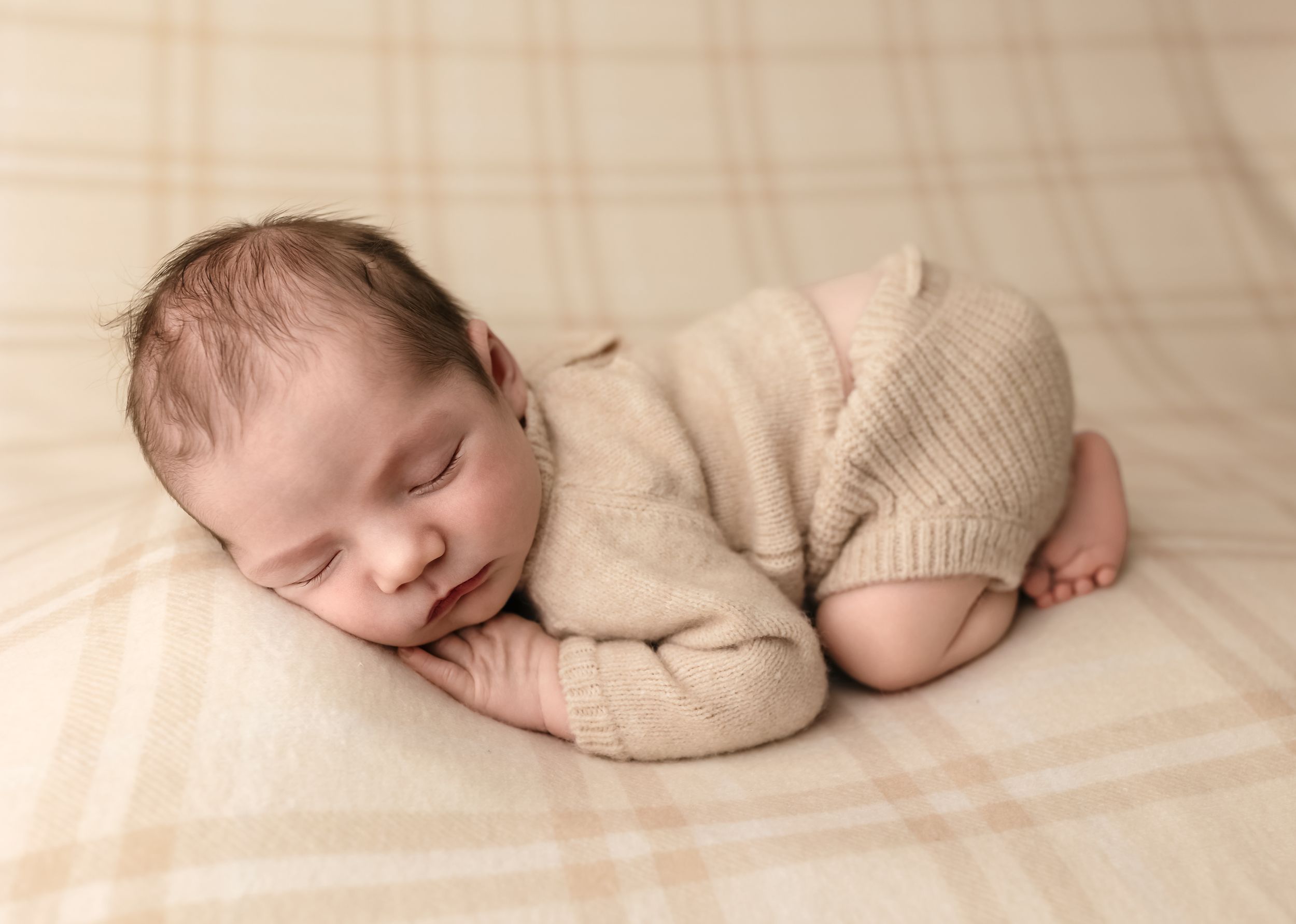 Baby boy dressed in a beige knit sweater sleep against a soft plaid blanket in bum up pose, by Charlottesville newborn photographer.
