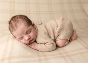 Baby boy dressed in a beige knit sweater sleep against a soft plaid blanket in bum up pose, by Charlottesville newborn photographer.