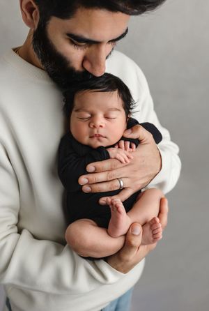 Dad cradles his new baby girl and kisses her on the head, captured by Charlottesville family, maternity, and newborn photographer.