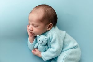 Baby boy in ice blue knits snuggles a blue teddy bear against a blue backdrop, captured by Charlottesville newborn photographer.