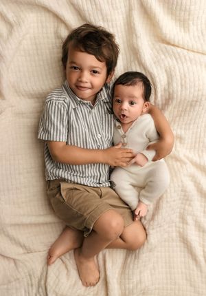 Toddler brother snuggles his new baby sister as they stick out their tongues together, captured by Charlottesville newborn photographer.