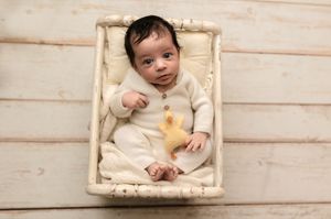 Bright-eyed newborn girl in white knits looks quizzically at the camera, captured by Charlottesville baby and newborn photographer.