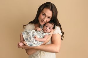 Beautiful mama holds her new baby girl, both dressed in summery, white dresses, captured by Charlottesville newborn nd family photographer.